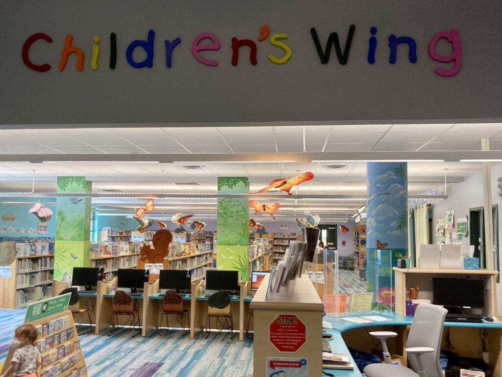 the children's wing at the safety harbor library with the words 'children's wing' on the wall on top and the librarian desk below