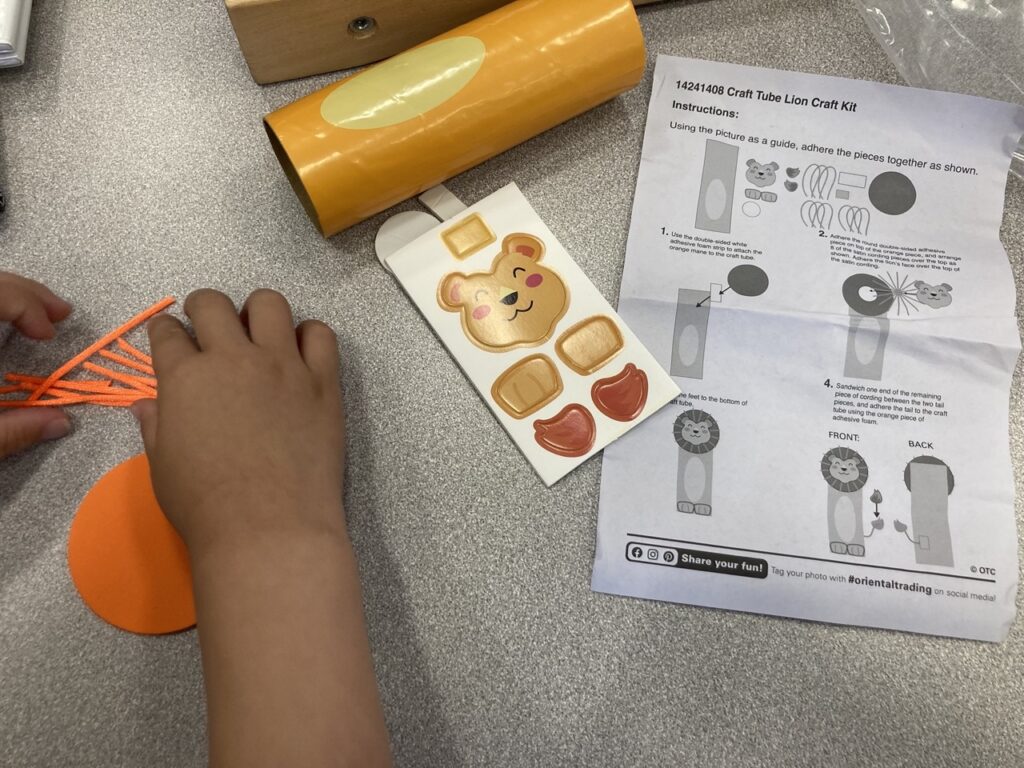 little kid's craft at the oldsmar library showing a toddler hand and orange craft pieces