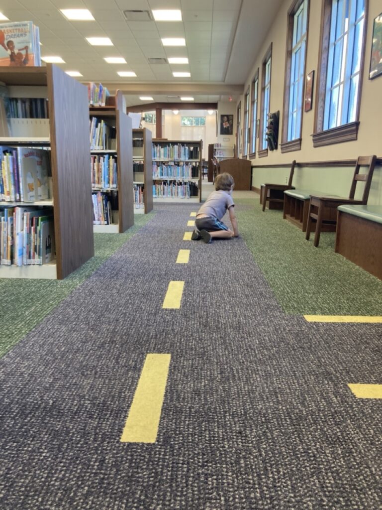 toddler in the distance sitting on carpet that looks like a road at the oldsmar library