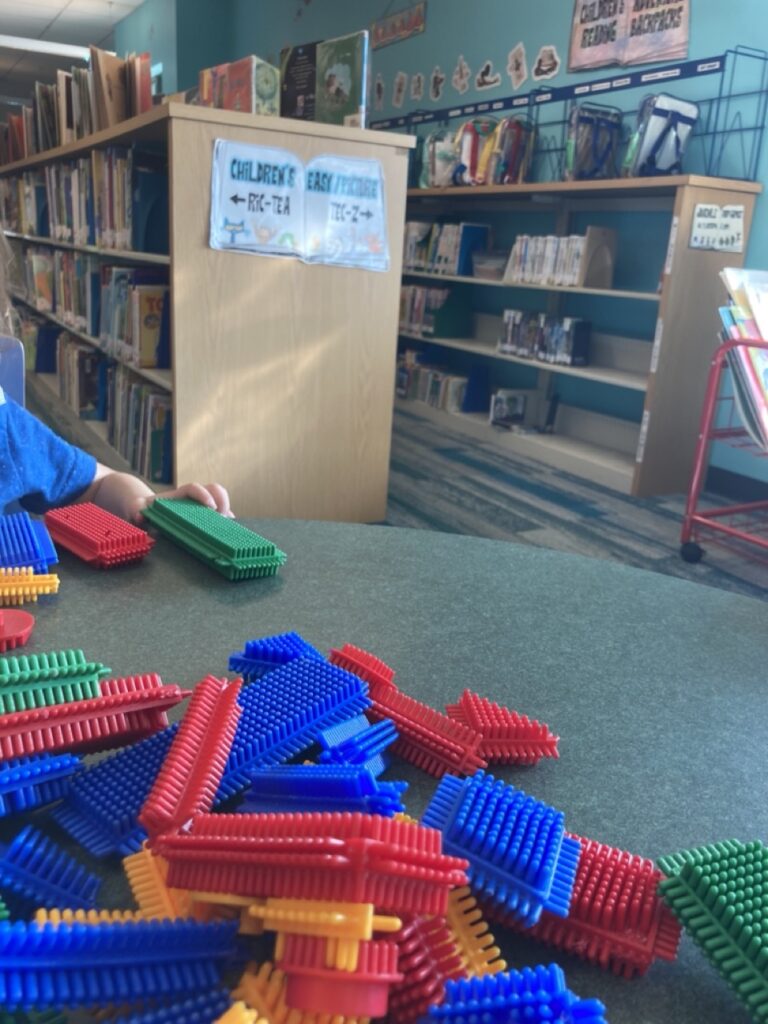 bristle blocks in the foreground on a table with children's library book shelves in the background