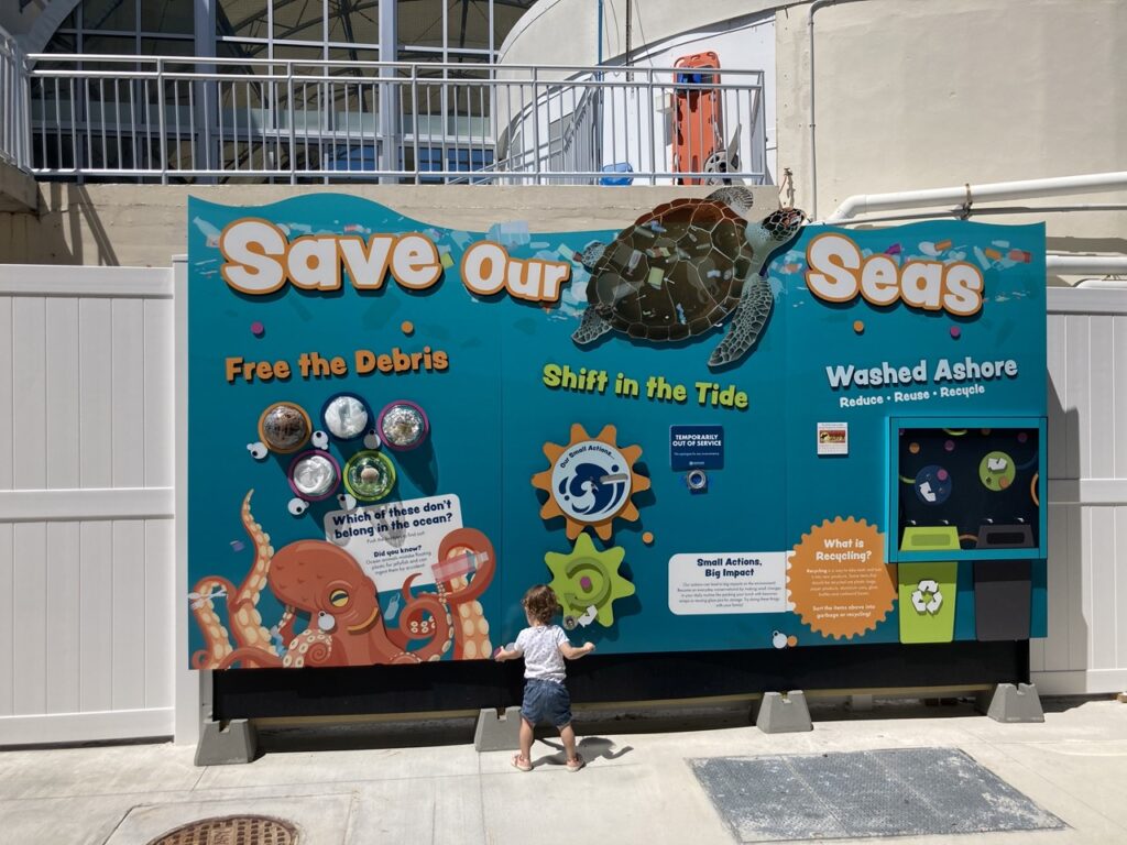 save our seas information sign at the clearwater marine aquarium with a baby standing in front of it