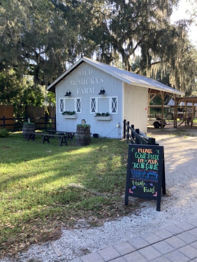 entrance of old mcmickys farm showing a white farm building that says old mcmickys farm and an entrance chalkboard sign