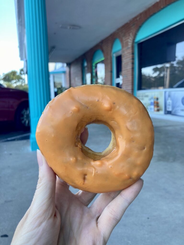 Hand holding a donut with orange frosting
