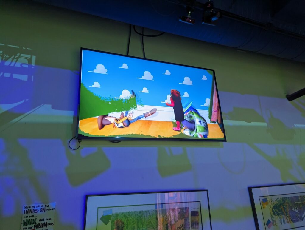 TV showing a green screen of a toy story background and a toddler standing in the picture