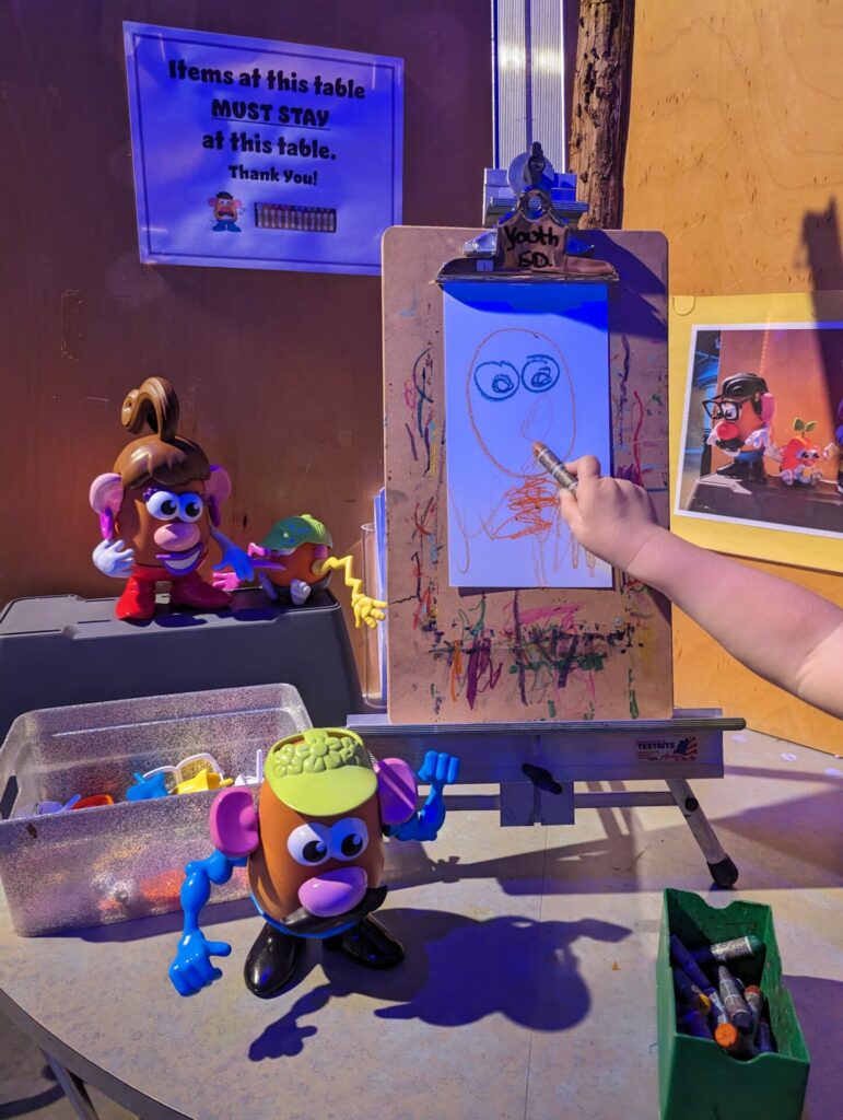A child's hand painting at an easel with mr. potato head pieces around the table