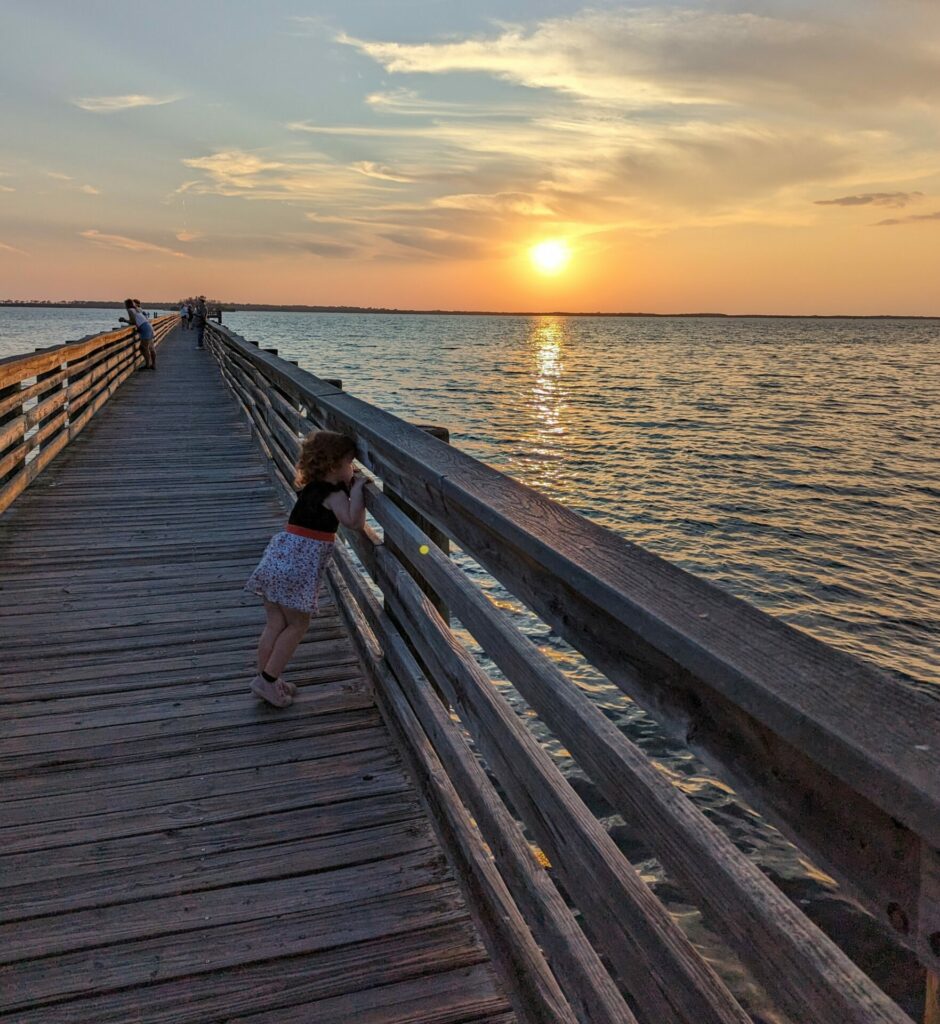child looking out the side of a pier at sunset