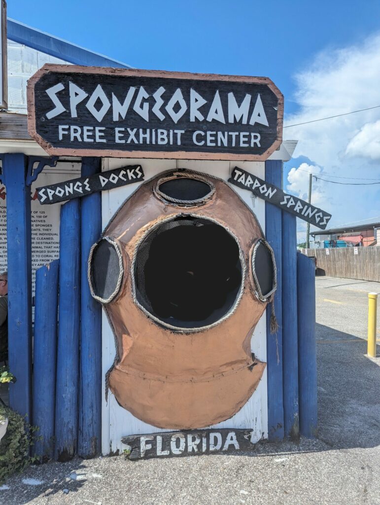 A sign on a fence of a sponge diver helmet with a sign that says spongeorama tarpon springs