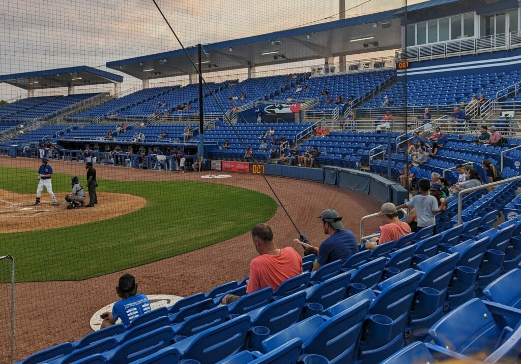 A picture from the bleachers at a minor league baseball game with the batter on the far left and mostly empty seats on the right side of the frame