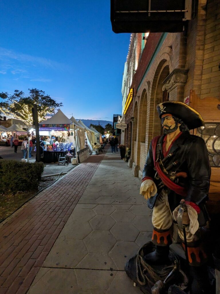 pirate statue on the sidewalk at amelia island with a market in the far distance