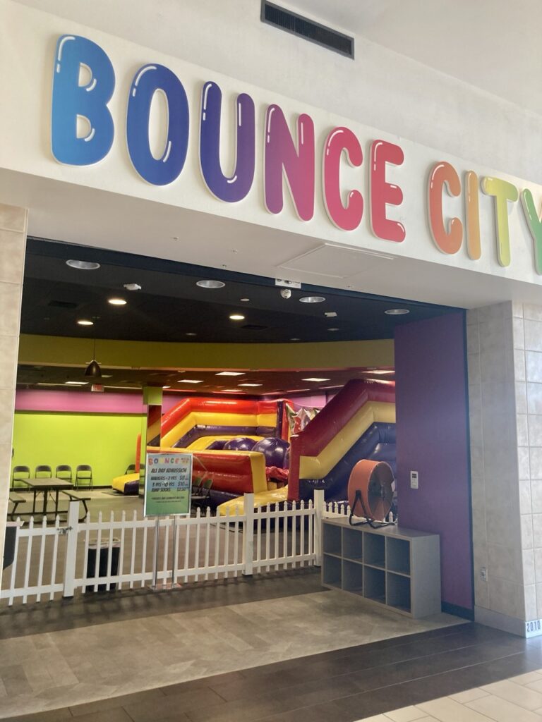 entrance to bounce city in clearwater fl, with a rainbow sign that says bounce city and bounce houses in the background