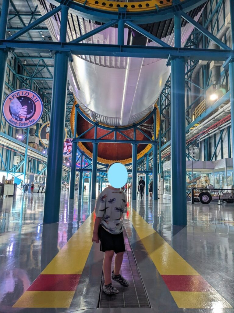 a toddler (with face obscured) standing under the Saturn V rocket at Kennedy space center