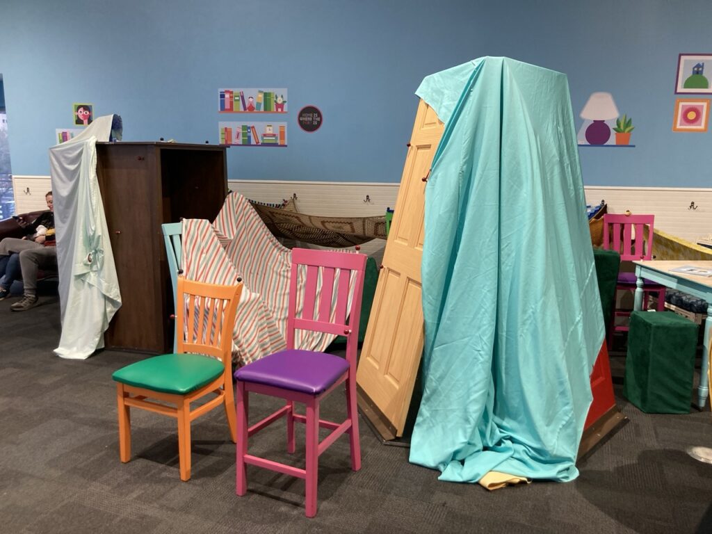 A fort building area at a children's museum with sheets and chairs and doors around to build forts with