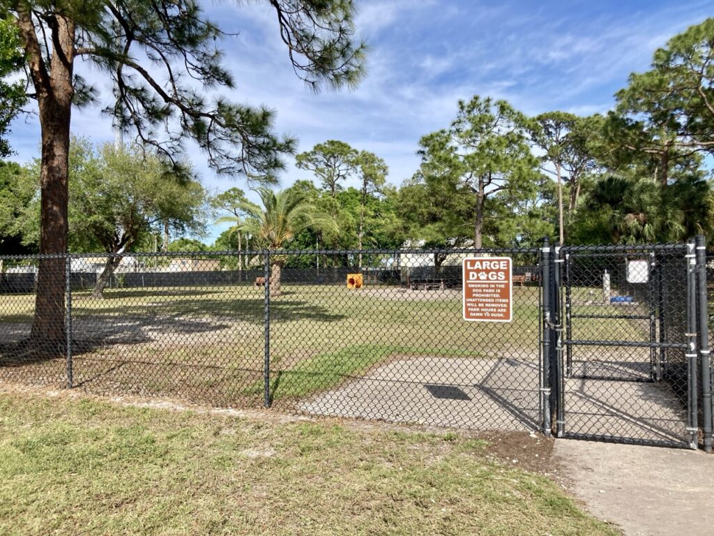 a dog park with a fence around it, palm trees, and a sign that says large dog area at freedom lake park in pinellas park
