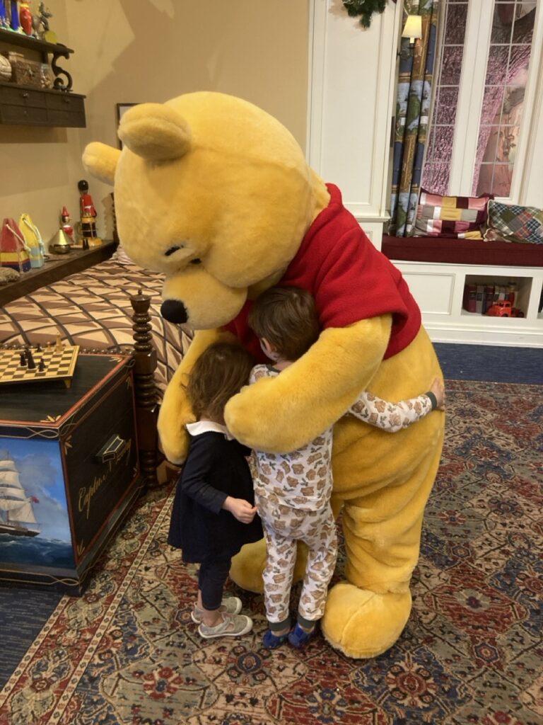 Pooh bear character hugging a toddler and preschooler