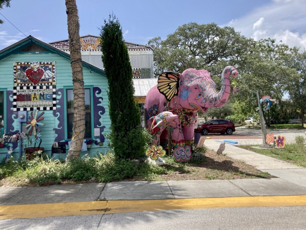 A big pink elephant statute with art designs and a building with art on the side at the Safety Harbor Art and Music Center