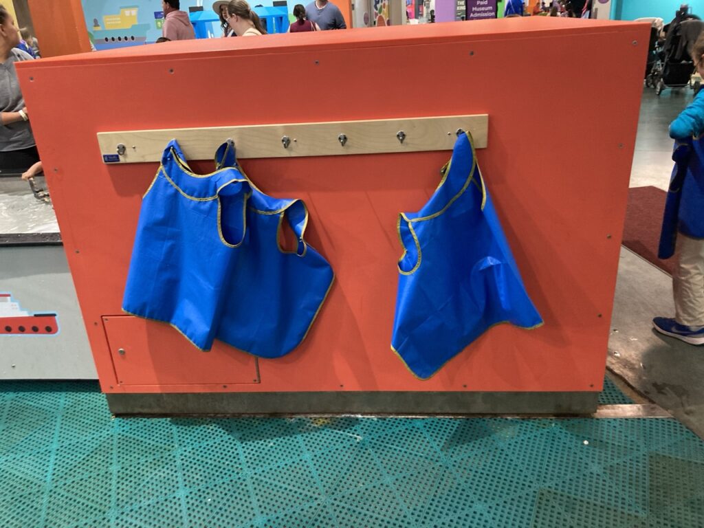 Water proof blue vests for kids hanging against an orange wall