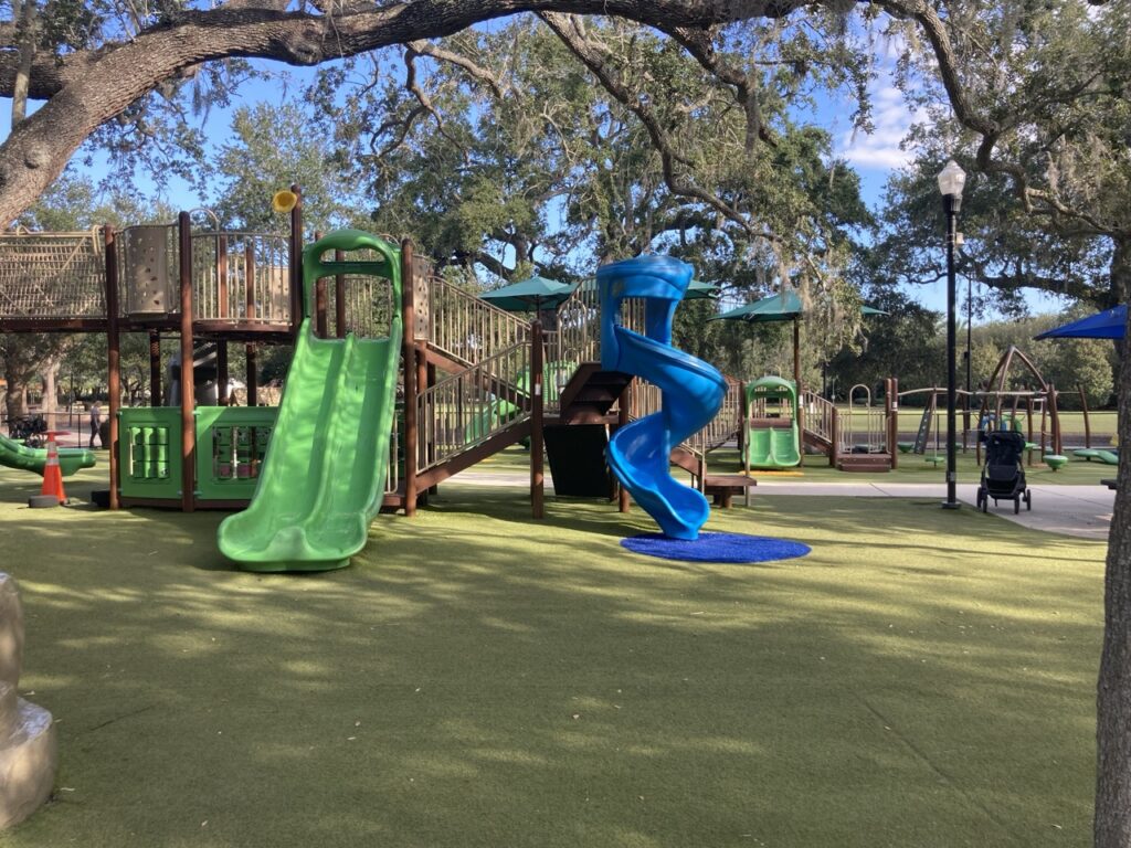 Outdoor playground under trees with a green and blue slide at Largo Central Park