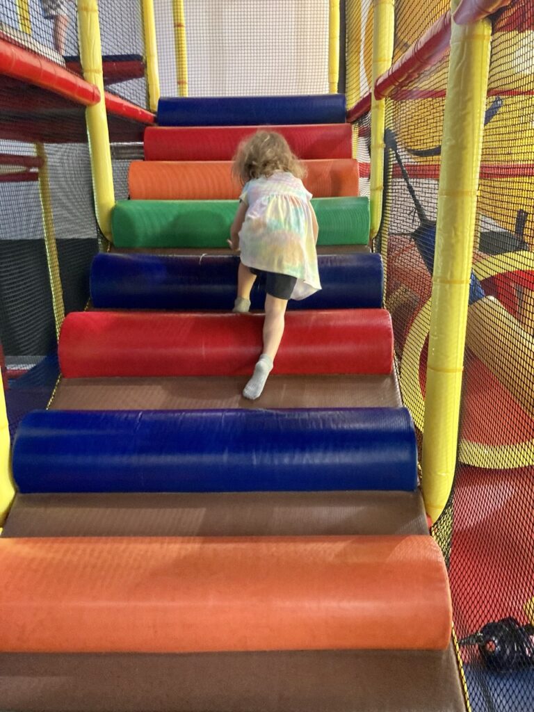 toddler climbing up a colorful foam stair ramp at an indoor playground
