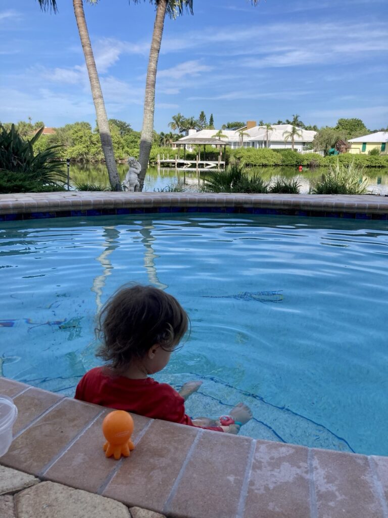 toddler sitting on the first step of a pool looking out