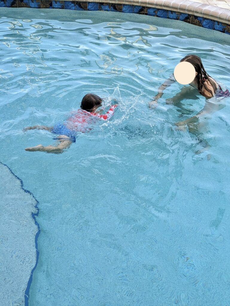 toddler with head under water in a pool swimming to an adult with their face obscured