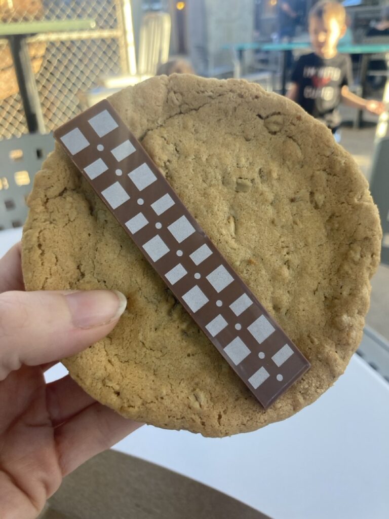a wookie cookie at hollywood studios held up by a hand. large cookie with a chocolate bar on it to look like a star wars belt
